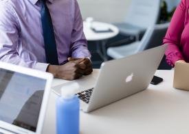 man in tie sitting in front of a laptop talking to a woman