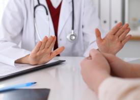 A doctors hands resting on a table across from a patient