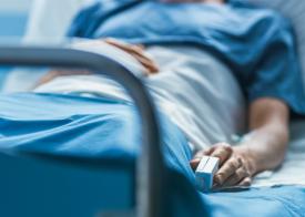 Patient lying in hospital bed with an oxygen monitor on finger